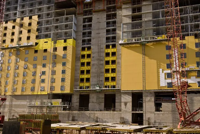 High-rise hotel under construction with yellow sheathing panels and scaffolding in place.