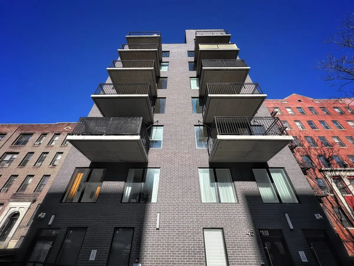 Modern multifamily building with dark brick facade and projecting concrete balconies designed for durability in high-traffic urban environments