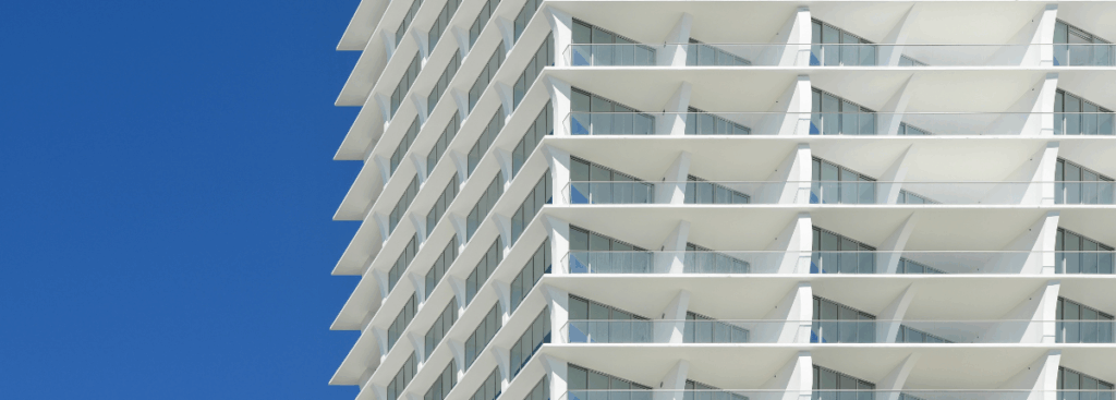 White high-rise facade with balconies against a clear blue sky, showing exterior coating performance in bright sunlight