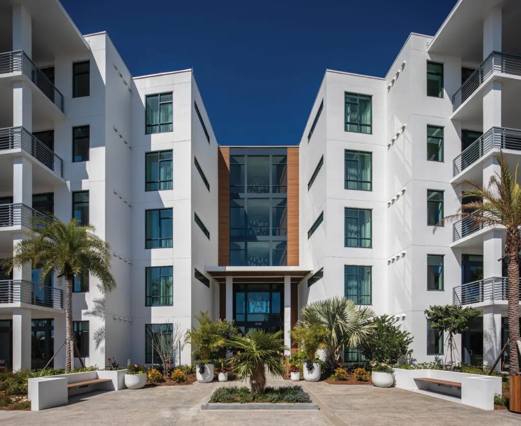 White multi-story building exterior with balconies and palm trees under bright sun. Evermore