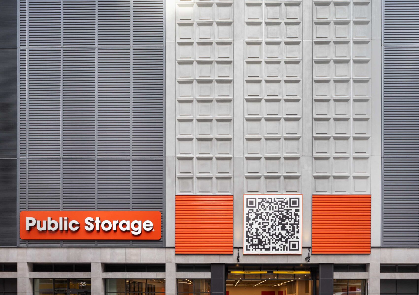 Public Storage building façade featuring gray metal panels, geometric wall textures and bright orange accent panels