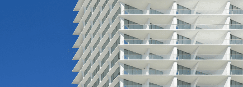 White high-rise facade with balconies against a clear blue sky, showing exterior coating performance in bright sunlight