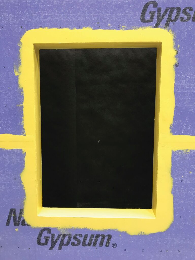 Window rough opening flashed with a yellow liquid-applied detail component that wraps into the opening and ties into treated sheathing joints